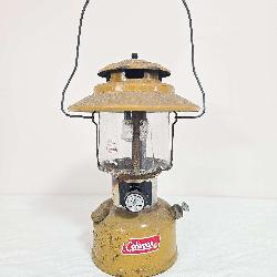 Vintage Coleman Model 228H Gold Bond double-mantle lantern with yellow/gold painted fount, matching yellow/gold porcelain ventilator, clear glass globe and wire bail handle. Marked 5/73. Shows paint w