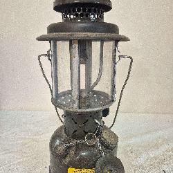 Coleman U.S. Army SMP lantern marked 1963 with dark military-style fount, dark ventilator, clear globe, wire frame and chained cap assembly. Shows substantial paint loss, oxidation and age-related wea