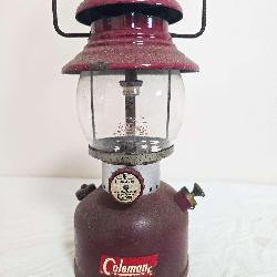 Coleman Model 200A pressure lantern with dark maroon fount and red/maroon porcelain ventilator, clear Coleman globe and wire bail handle; marked 1/62. Shows decal wear, surface wear and age-related us