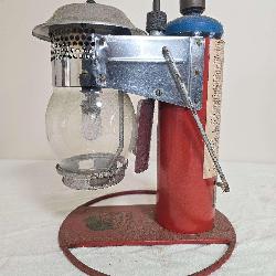 Clayton & Lambert Mfg. Co. propane lantern with red base and upright fuel-cylinder housing, silver-tone lantern assembly, clear globe and blue-topped propane cylinder as shown. Shows paint wear, oxida