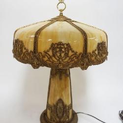 ORNATE ANTIQUE SLAG GLASS TABLE LAMP, METAL IMAGES OF WINGED GRIFFINS & WOMAN BUST, INTERIOR LIT SLAG GLASS BASE, CURVED SLAG GLASS PANELS ON SHADE, APPROXIMATELY 18 IN X 26 IN HIGH