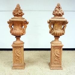1151	OUTSTANDING PAIR OF TERRA COTTA URNS ON PEDESTALS WITH LIDS, EACH FLANKED WITH WINGED CHERUBS ON SIDES, APPROXIMATELY 24 IN X 19 IN X 72 IN H OVERALL
